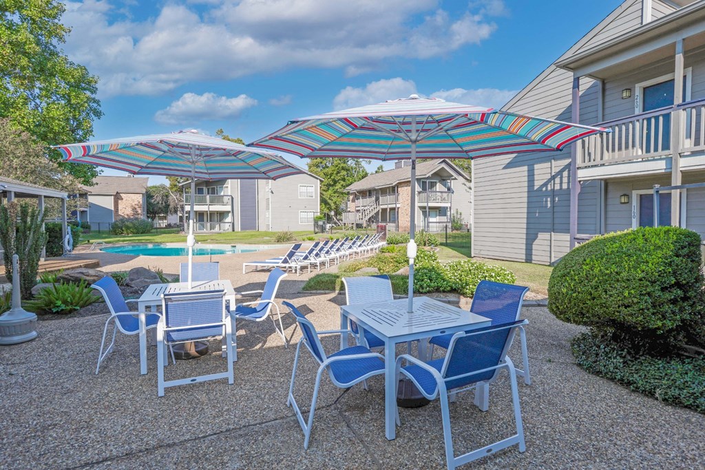 Poolside seating with a table and chairs under a striped umbrella at Laurel Parc apartments in Shreveport, LA.