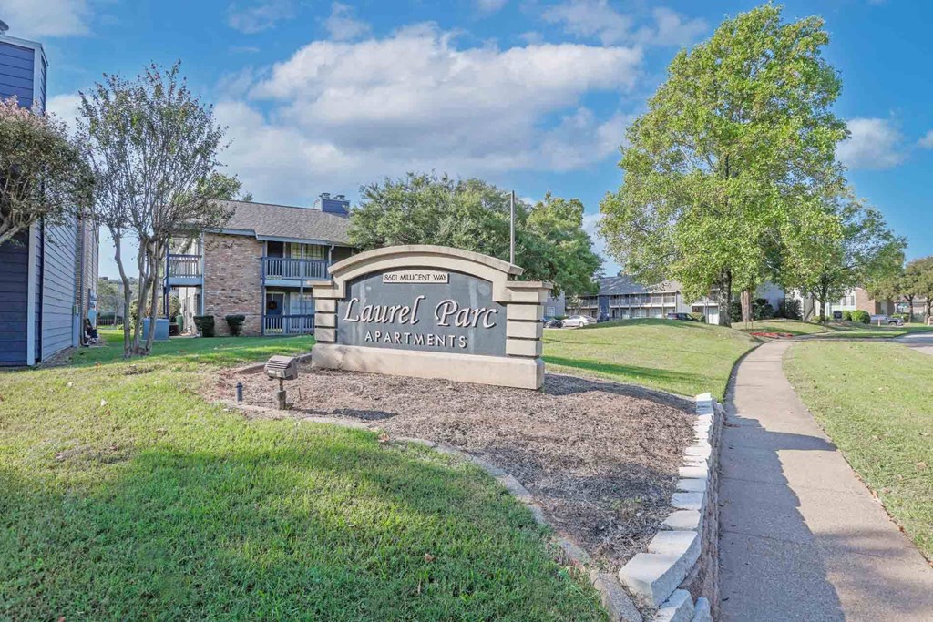 The entrance sign to Laurel Park Apartments is surrounded by a well-maintained lawn and trees at Laurel Parc apartments in Shreveport, LA.