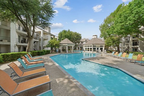 A pool surrounded by lounge chairs and trees.