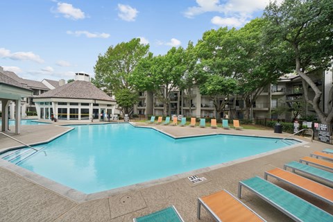 A large swimming pool surrounded by sun loungers and trees.