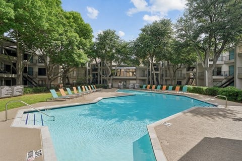 A swimming pool surrounded by trees and chairs.