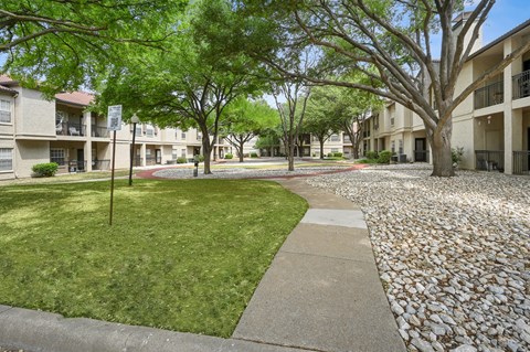 View of walk path covered by trees at La Costa Apartments in Plano, TX