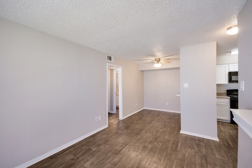 an empty living room and kitchen with wood flooring and a ceiling fan