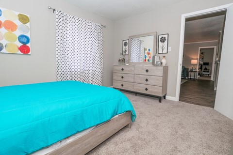 A cypress bedroom with a teal bedspread and a white dresser with mirror at The Marq in Shreveport, LA