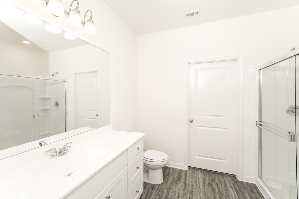 a bathroom with a shower, big mirror and white cabinets