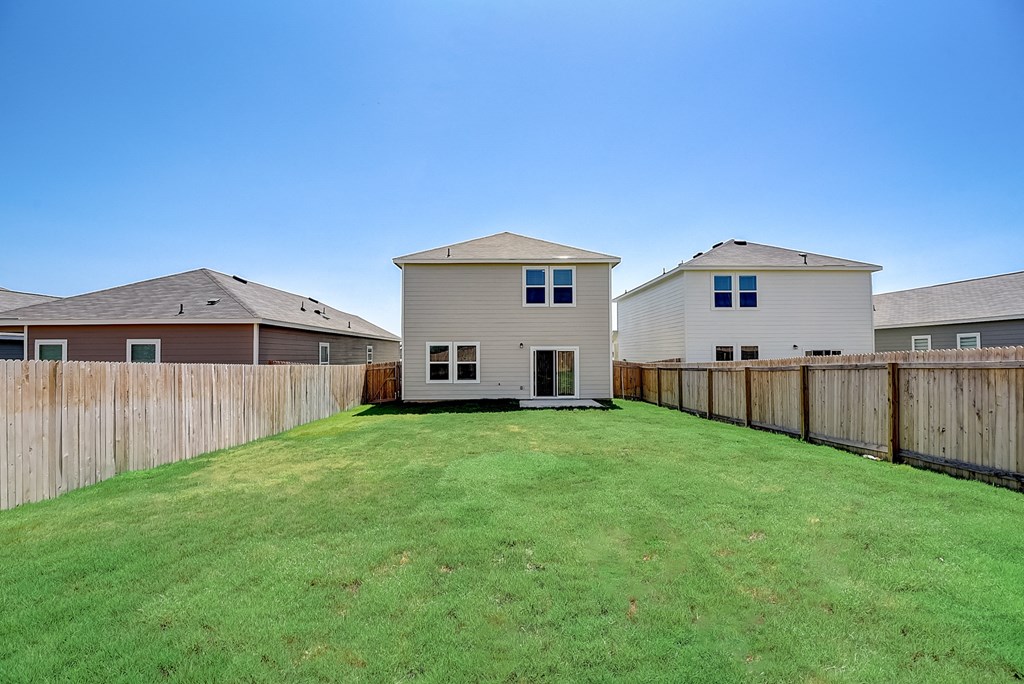 a backyard with a fence and two houses in the background at Beacon at Meridian, San Antonio, TX