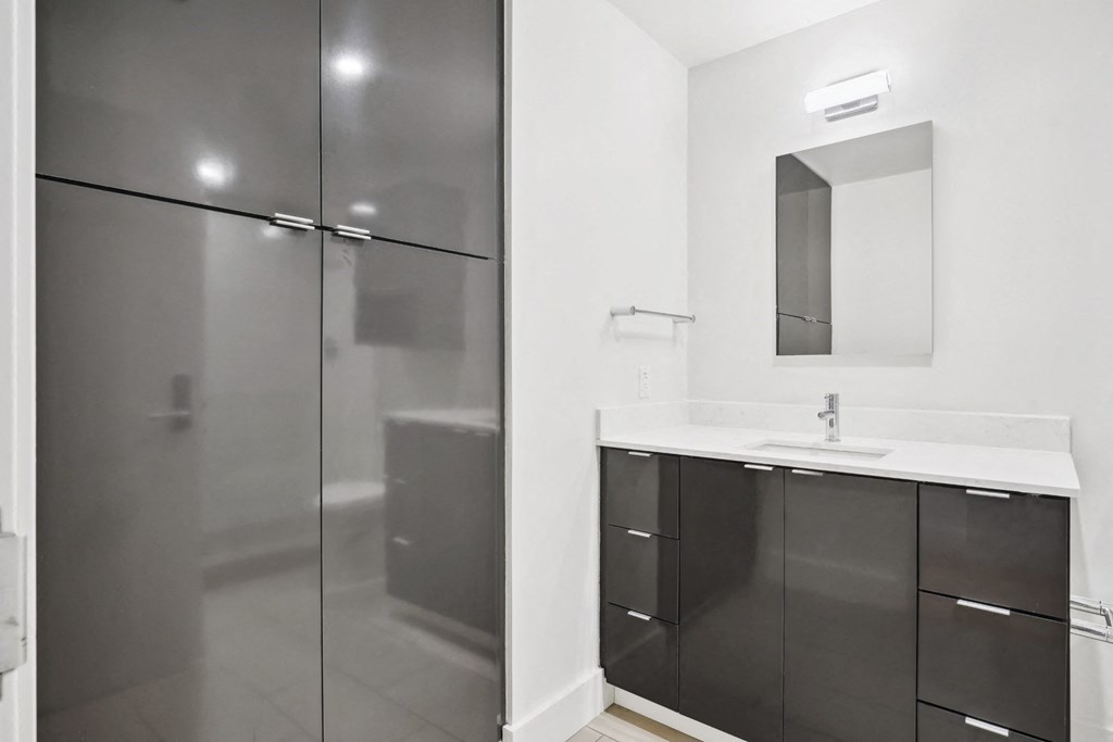 Sleek bathroom with walk-in shower, modern vanity with white countertop and black cabinets at Mid Elm Lofts in Dallas, TX