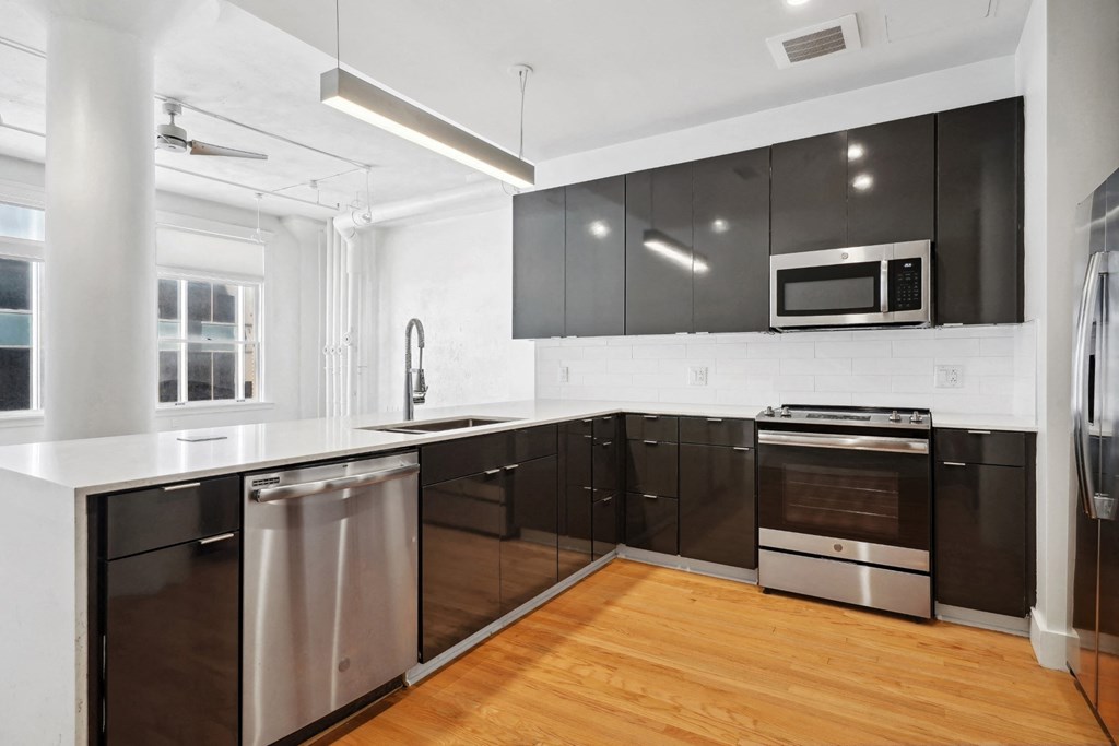 View from inside kitchen with microwave, dishwasher and stove/oven. Black cabinetry provides beautiful contrast to the white countertops. Mid Elm Lofts in Dallas, TX