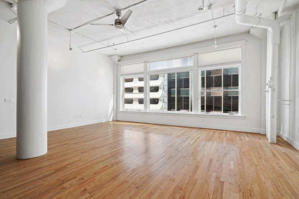 Large living room with polished wood floors, large windows, and a ceiling fan at Mid Elm Lofts in Dallas, TX