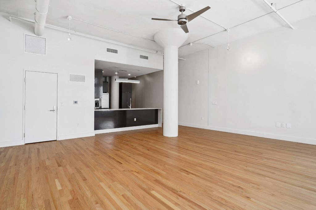 Standing in the living area looking toward the kitchen with a ceiling fan overhead and polished wood floors below at Mid Elm Lofts in Dallas, TX