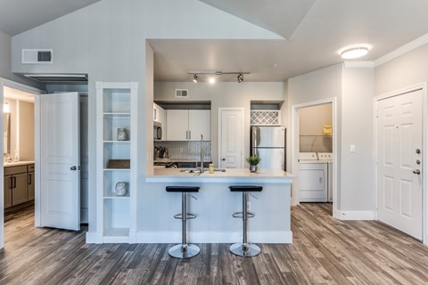 A kitchen with white cabinets and a bar area with two stools.