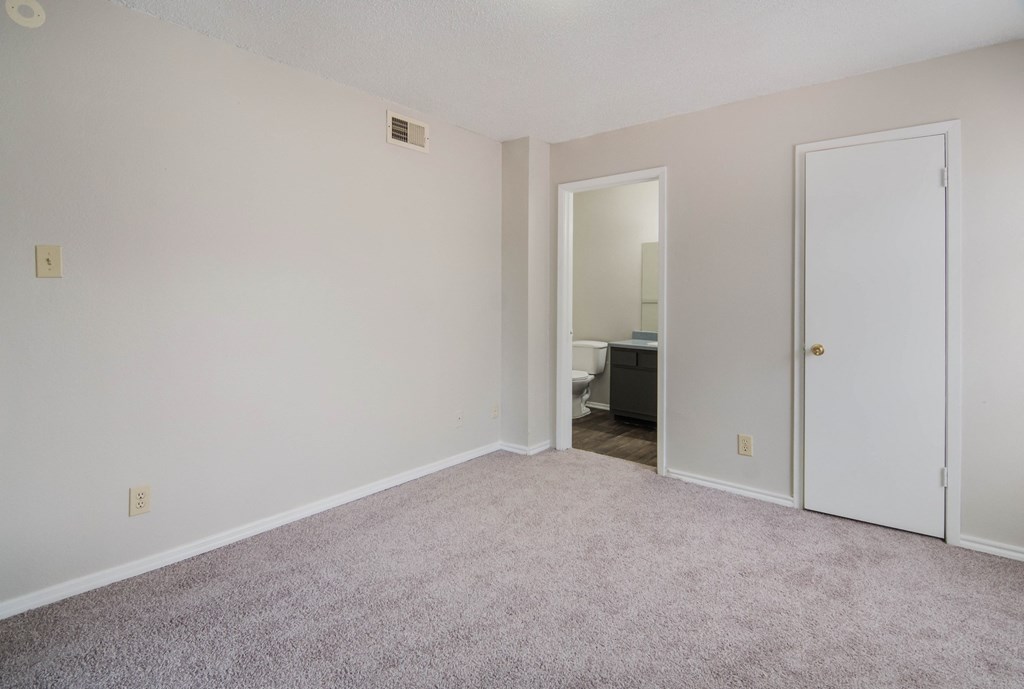 an empty living room with carpet and a door to a bathroom