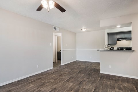 an empty living room with a kitchen and a ceiling fan