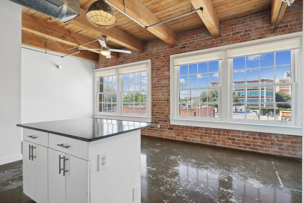 View of kitchen island and living room with brick wall and large windows with scenic view | Deep Ellum Lofts in Dallas, TX