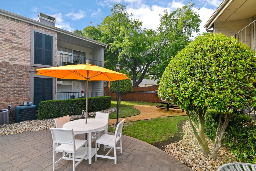 a patio with a white table with an orange umbrella and white chairs