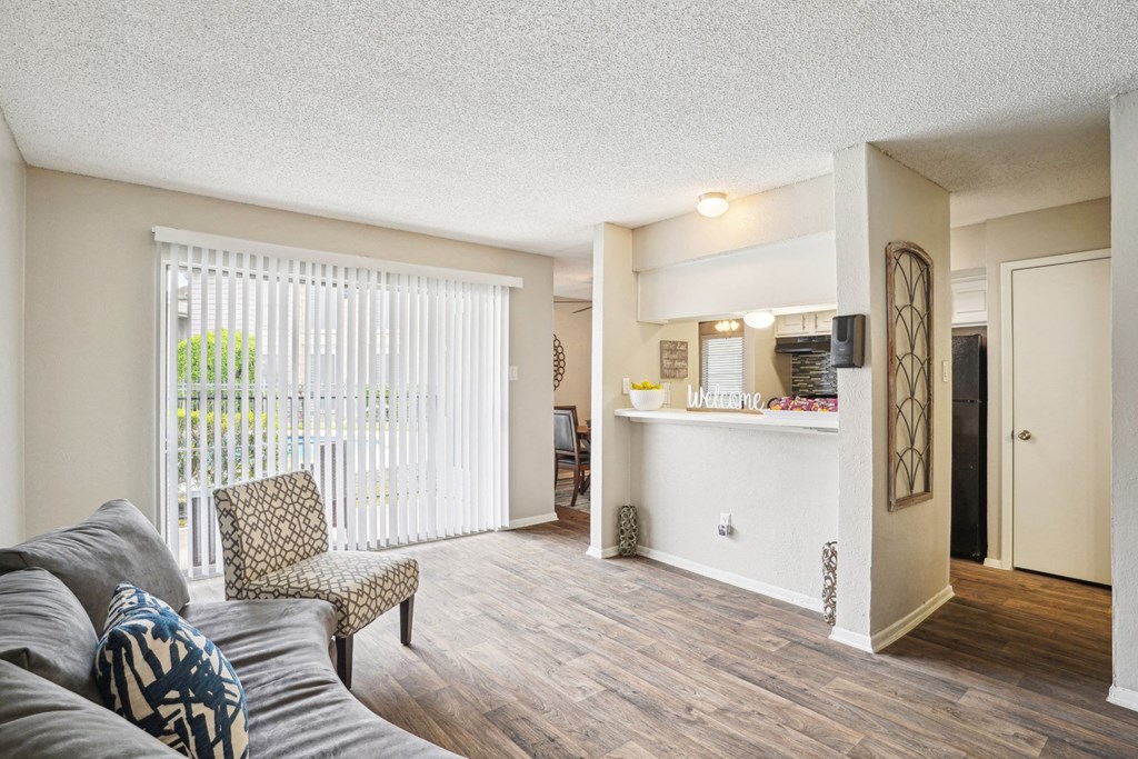 Model A2 floor plan living room with a couch, chair, door to balcony, and view of kitchen Noel on The Parkway in Dallas, TX