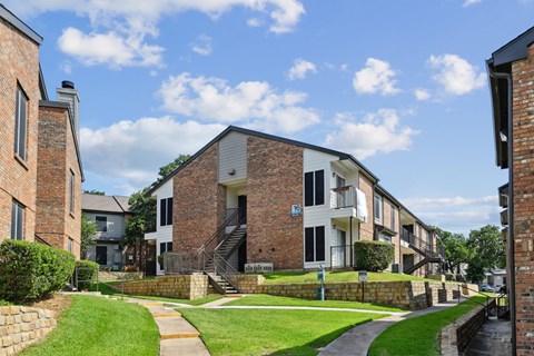 An apartment building with green lawns in front at The Oaks of Denton Apartments in Denton, TX