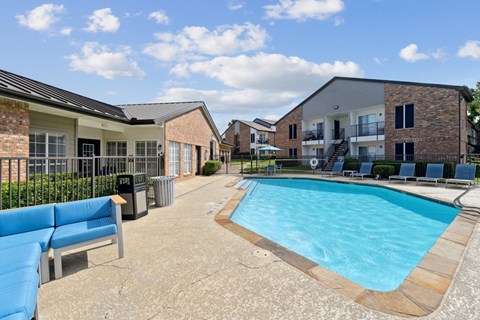A pool with comfortable lounge chairs and a bench at The Oaks of Denton Apartments in Denton, TX