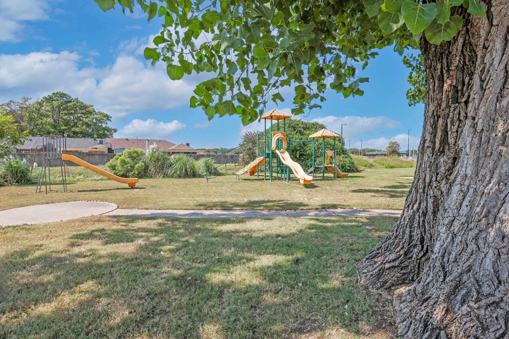 A playground with a slide and a tree in the foreground at Orleans Square in Shreveport, LA