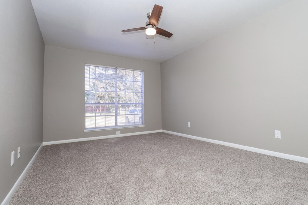 A bedroom with a ceiling fan, large window, and lush carpet at Orleans Square in Shreveport, LA