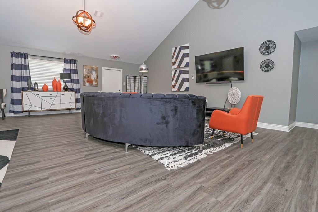 A clubhouse with a grey sofa, red chair, and TV at Orleans Square in Shreveport, LA