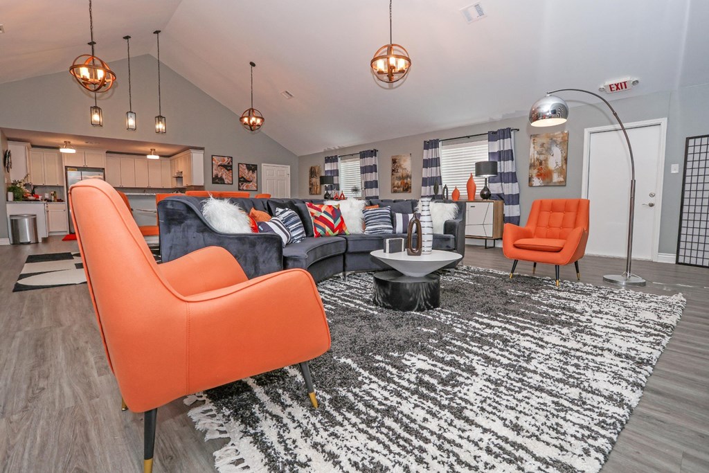 A clubhouse room with a black and white rug, orange chairs, and a kitchen area in the background at Orleans Square in Shreveport, LA