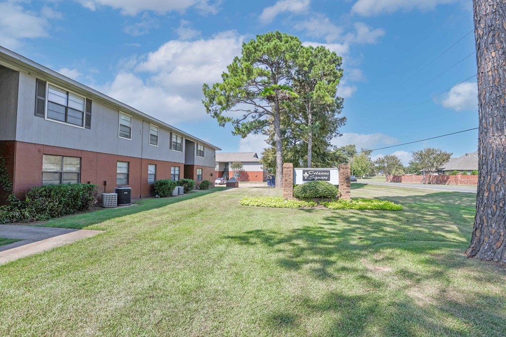 A tree stands in front of an "Orleans Square" sign and apartment buildings at Orleans Square in Shreveport, LA