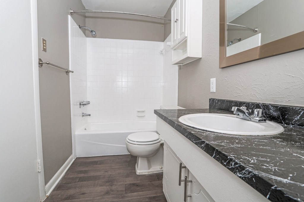 A bathroom with a marble counter, toilet, sink, and tub at Orleans Square in Shreveport, LA