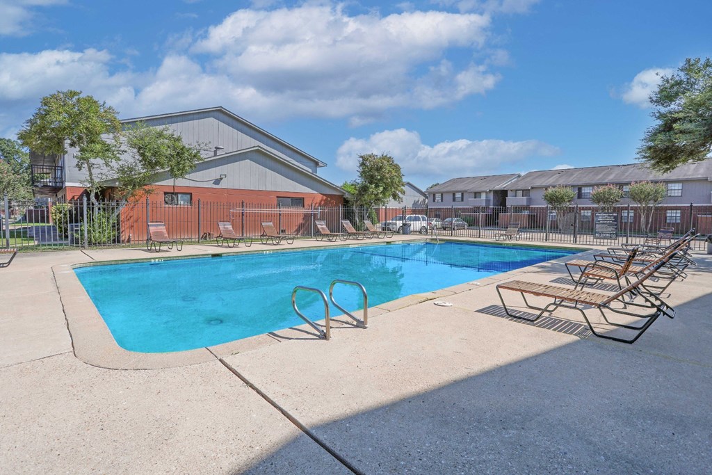 A swimming pool with chairs, a ladder, and apartment buildings in the background at Orleans Square in Shreveport, LA