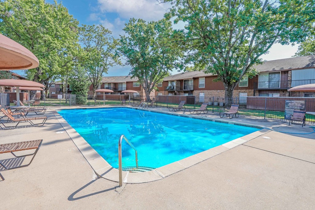 A partly shaded swimming pool surrounded by trees and chairs with umbrellas at Orleans Square in Shreveport, LA