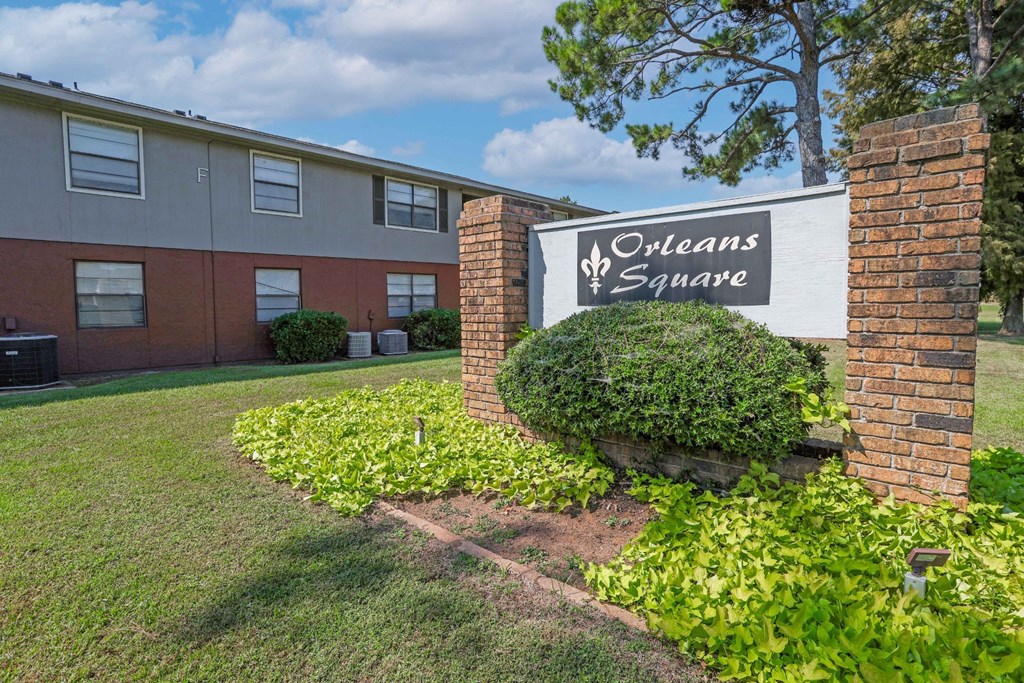 A sign for Orleans Square is surrounded by lush greenery in front of an apartment building at Orleans Square in Shreveport, LA