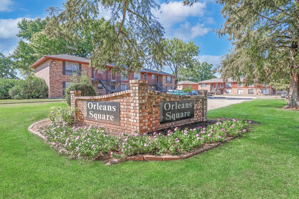 A brick sign that reads "Orleans Square" is surrounded by flowers and greenery at Orleans Square in Shreveport, LA