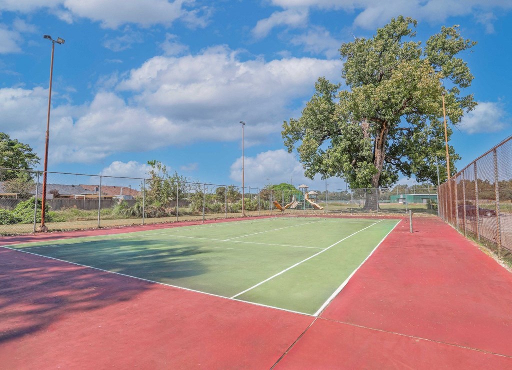 A fenced tennis court with a red and green surface and white lines at Orleans Square in Shreveport, LA