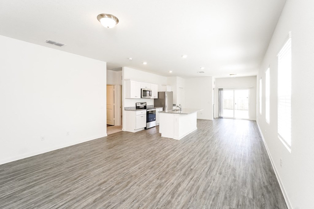 a spacious family living room with a kitchen and windows