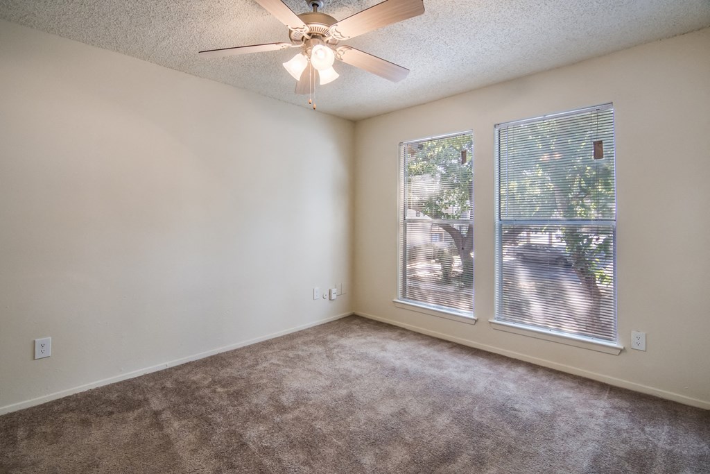 an empty living room with a large window and a ceiling fan