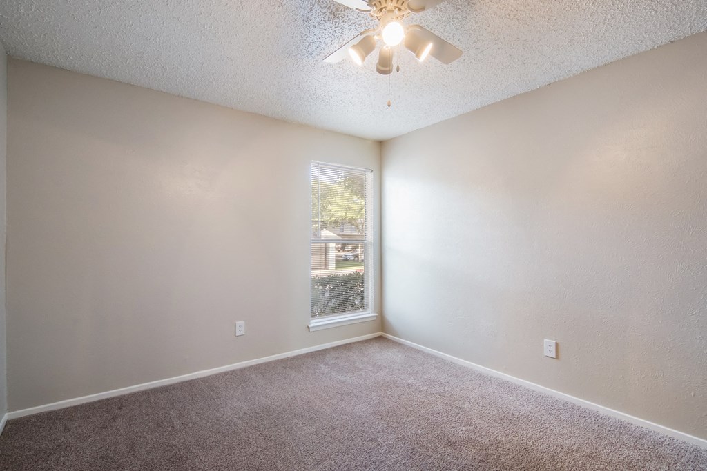 an empty bedroom with a ceiling fan and a window