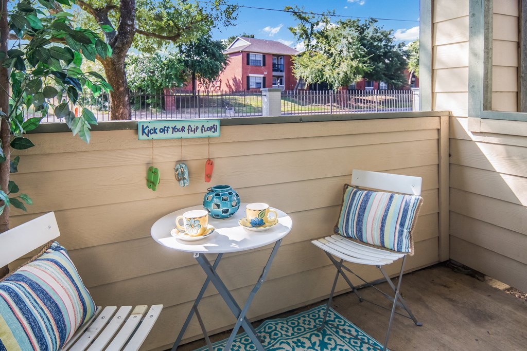 a balcony with two chairs and a table with two cups and a cake on it