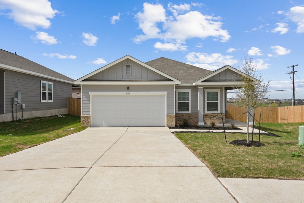 a house with a concrete driveway and a tree in the front yard at Beacon at Presidential Heights, Manor, TX