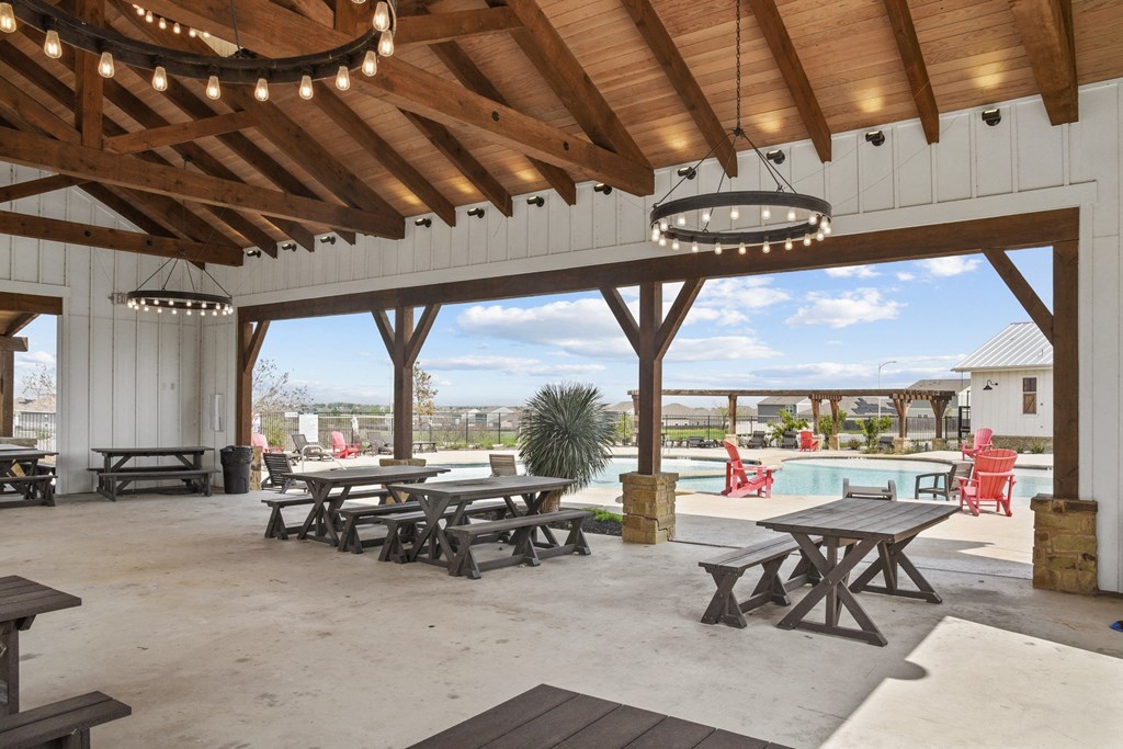 a covered patio with picnic tables and a pool in the background at Beacon at Presidential Heights, Texas, 78653