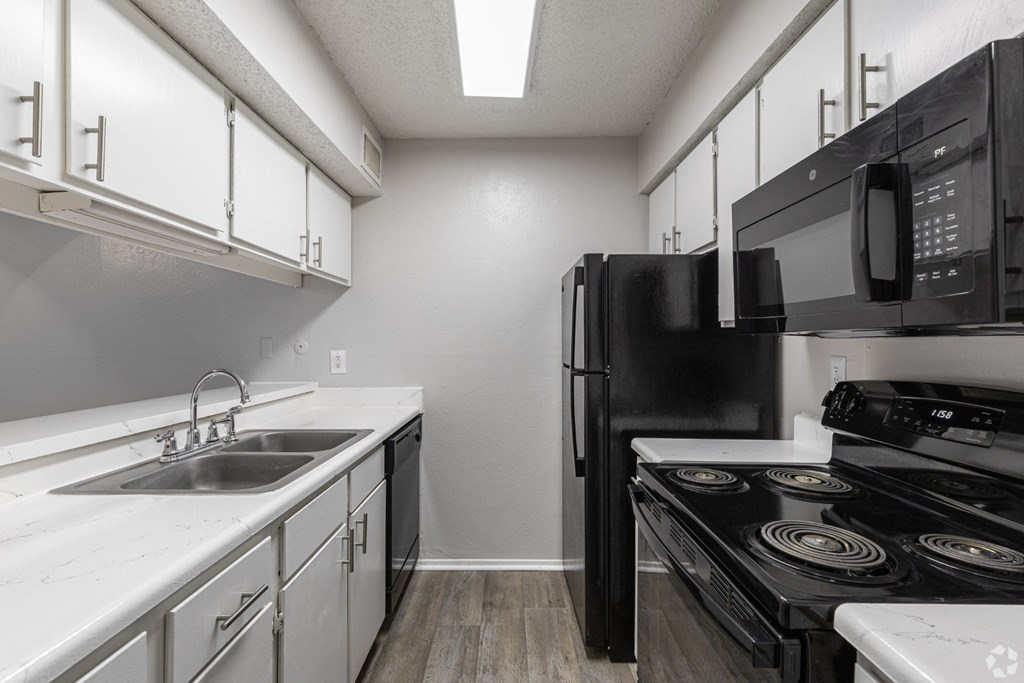A kitchen with black appliances and white cabinets at Preston Oaks Apartments in Dallas, TX.