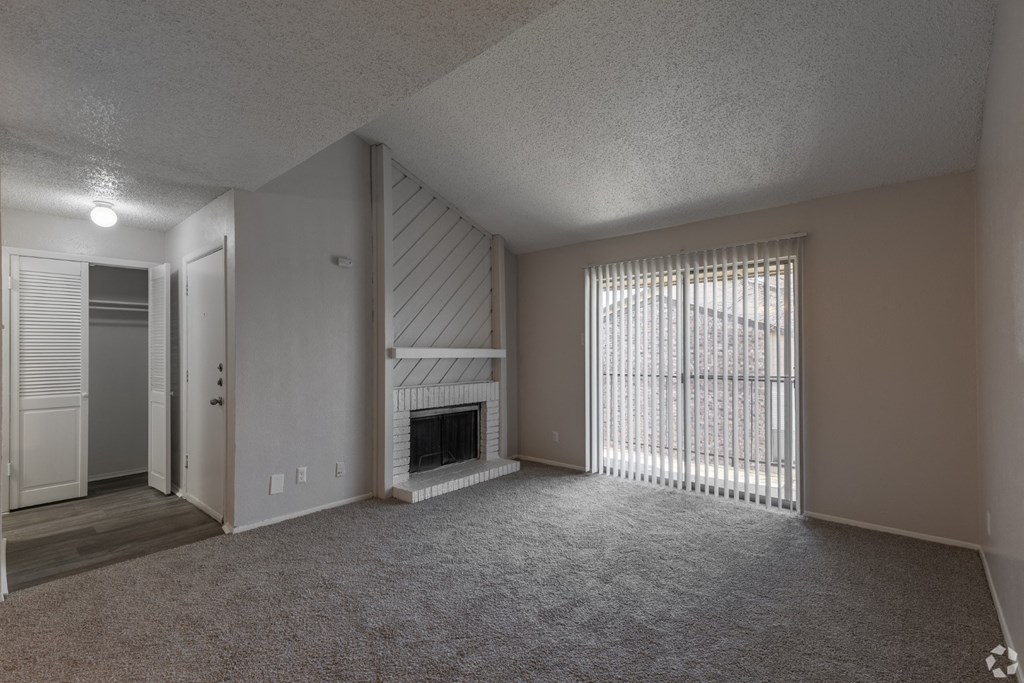 A living room with a fireplace, carpeted floor, and sliding glass doors at Preston Oaks Apartments in Dallas, TX.