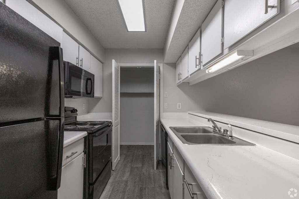 A black refrigerator is on the left in a kitchen with white countertops at Preston Oaks Apartments in Dallas, TX.