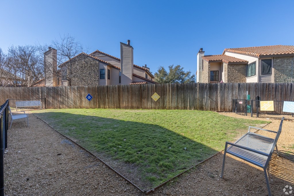 A dog park with a wooden fence and a bench at Preston Oaks Apartments in Dallas, TX.
