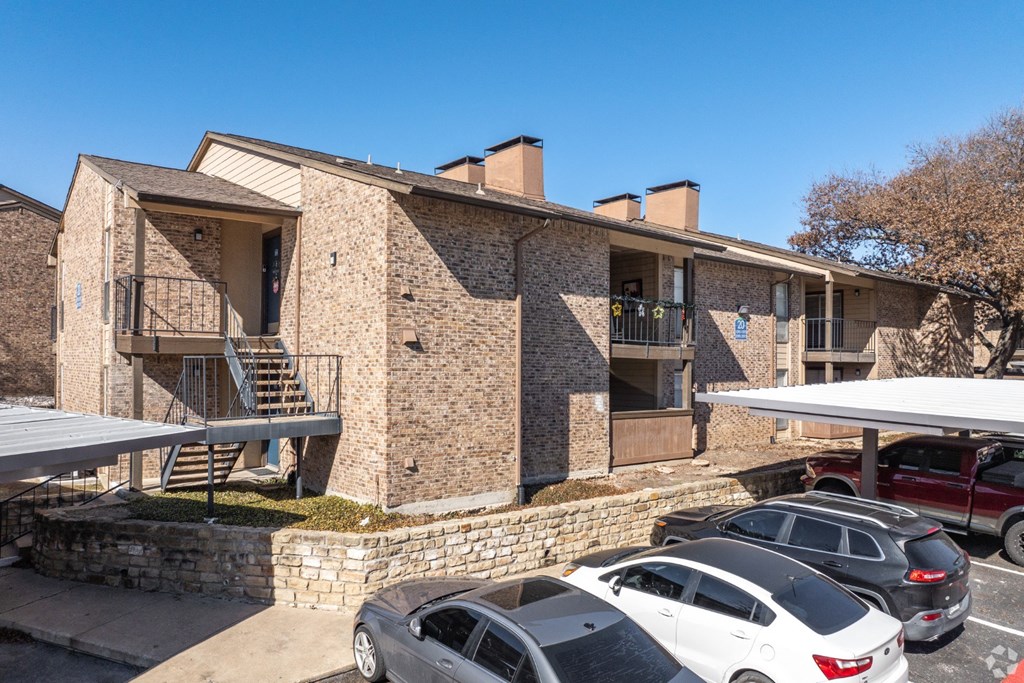 A stone apartment building with a parking lot in front at Preston Oaks Apartments in Dallas, TX.