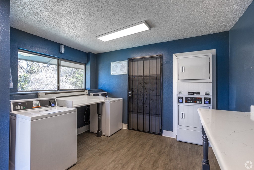 A laundry facility with washers, dryers, and a white folding table at Preston Oaks Apartments in Dallas, TX.