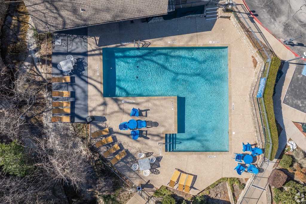 An aerial view of a pool with blue chairs and a table at Preston Oaks Apartments in Dallas, TX.