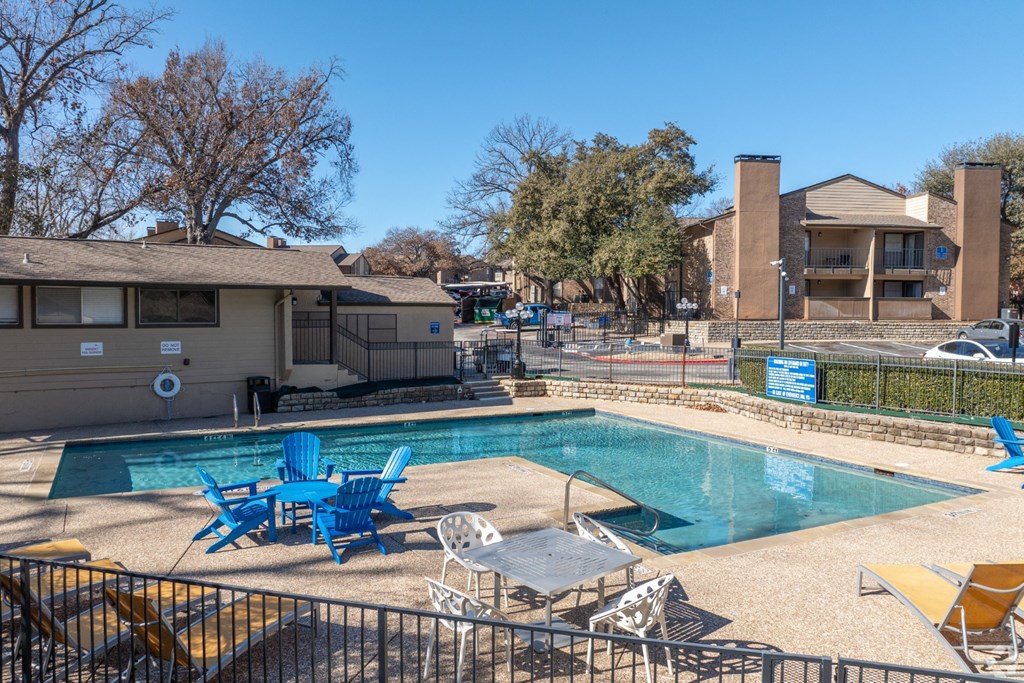 A pool with chairs around it and an apartment building in the background at Preston Oaks Apartments in Dallas, TX.