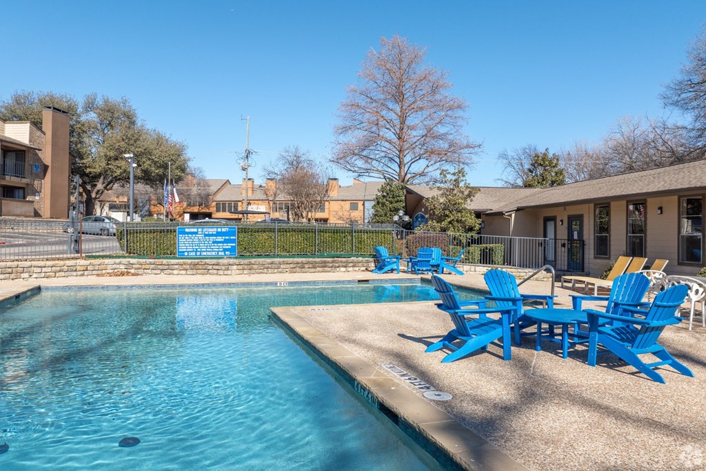 A pool with blue chairs a blue sky in the background at Preston Oaks Apartments in Dallas, TX.