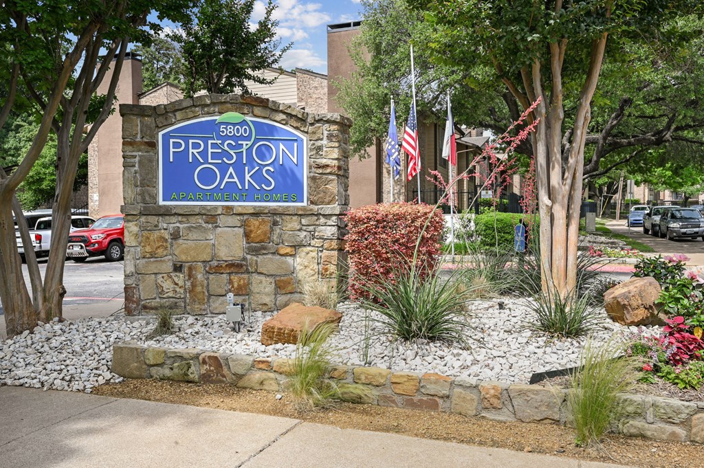 An entry sign in front of a stone building at Preston Oaks Apartments in Dallas, TX.