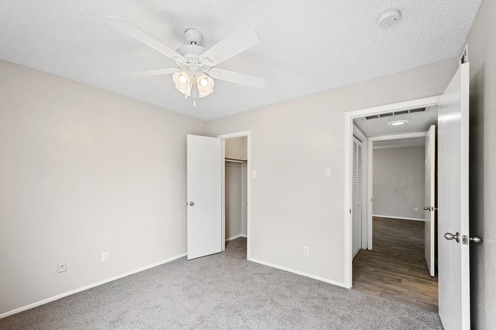 a bedroom with a ceiling fan and a hallway in the background